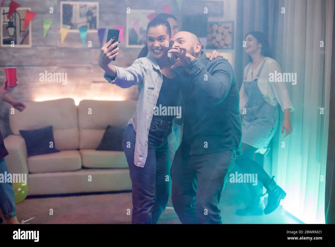 Man and beautiful woman using smartphone taking a selfie while partying with their friends. Stock Photo