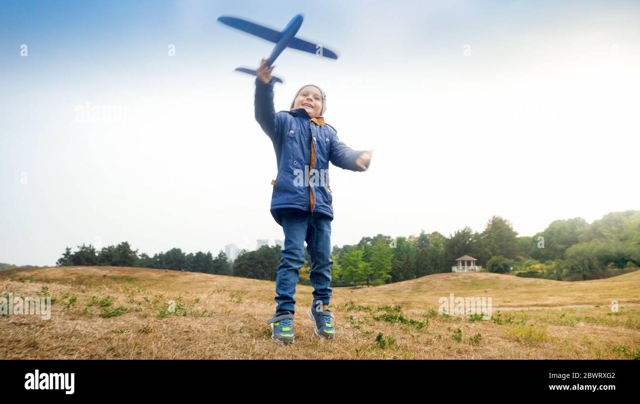Portrait of happy excited little boy launching and throwing toy airplane in the field Stock Photo