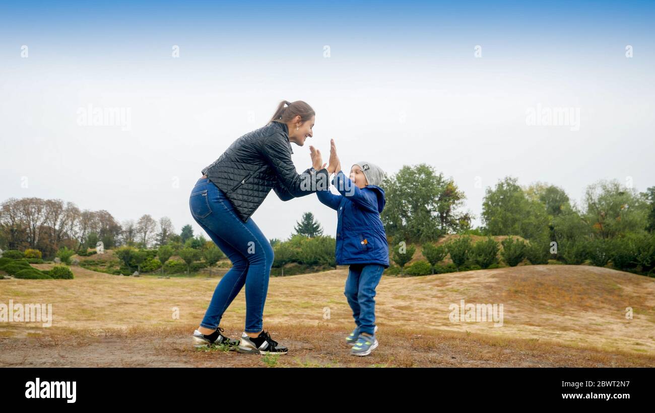 Happy smiling mother and little son standing on field and giving five each other Stock Photo