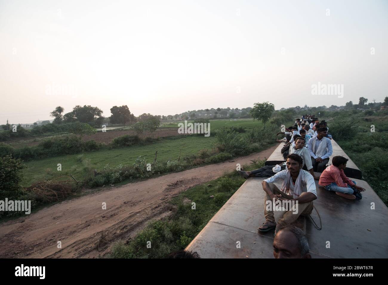 Men on top of overcrowded train passing through countryside in Madhya Pradesh, India. Indian Railways. Stock Photo