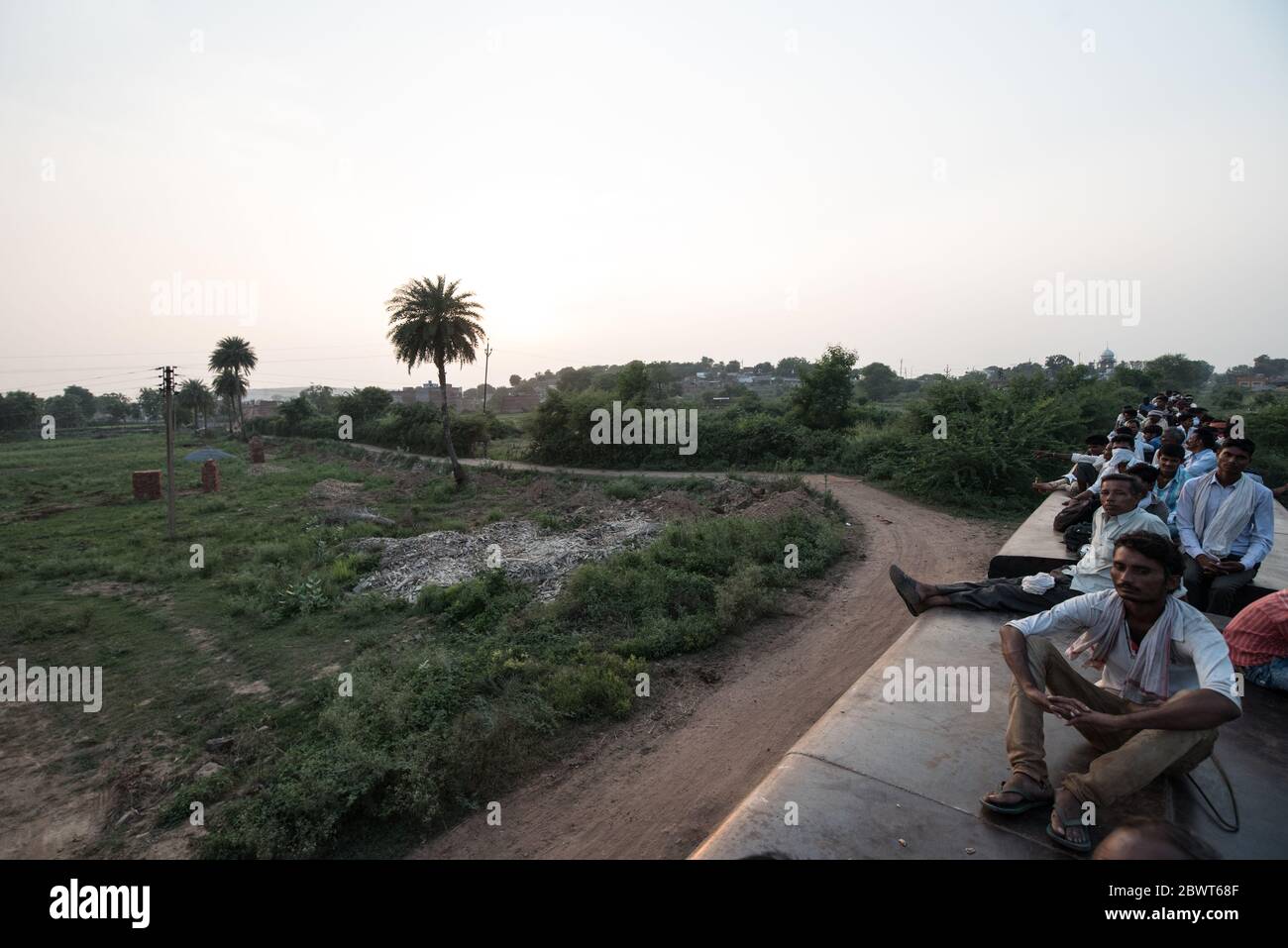 Men on top of overcrowded train passing through countryside in Madhya Pradesh, India. Indian Railways. Stock Photo