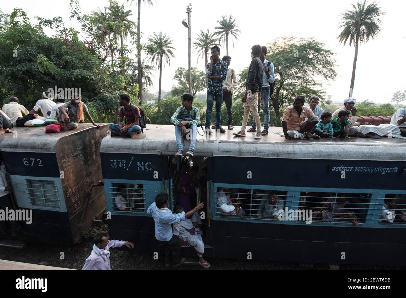 Passengers on top of overcrowded train at a train station in rural Madhya Pradesh, India. Indian Railways. Stock Photo