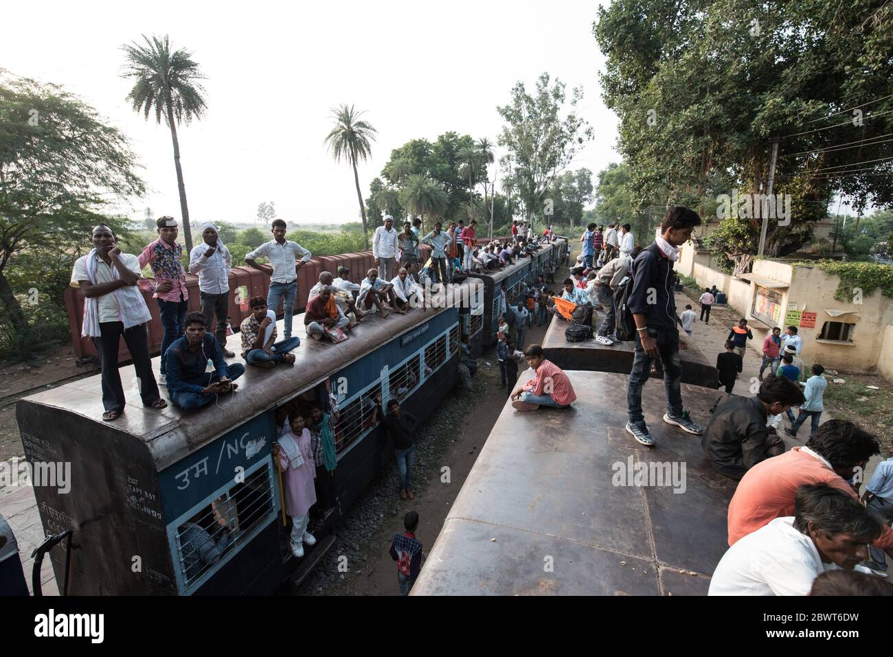 Passengers on top of overcrowded train at a train station in rural Madhya Pradesh, India. Indian Railways. Stock Photo