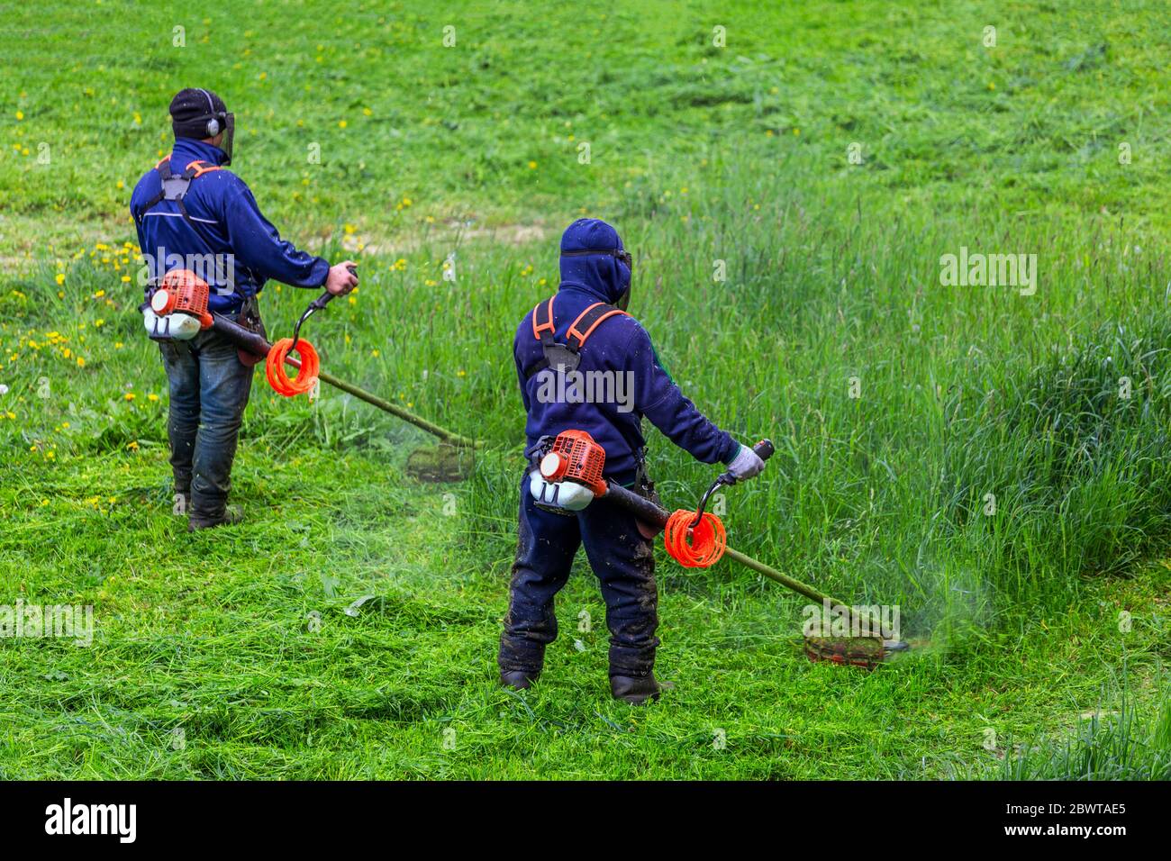 two lawnmower men with string trimmer and face mask trimmong grass - close-up Stock Photo