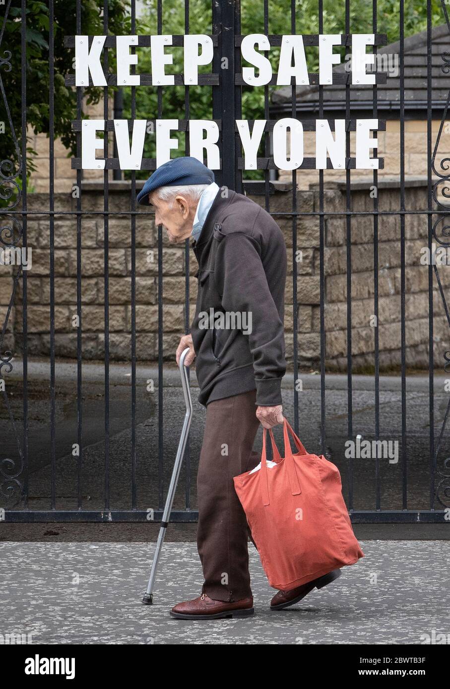 A pensioner walks past a sign that reads 'Keep Safe Everyone' in Leith, Edinburgh, as Scotland is moving into phase one of the Scottish Government's plan for gradually lifting lockdown. Stock Photo