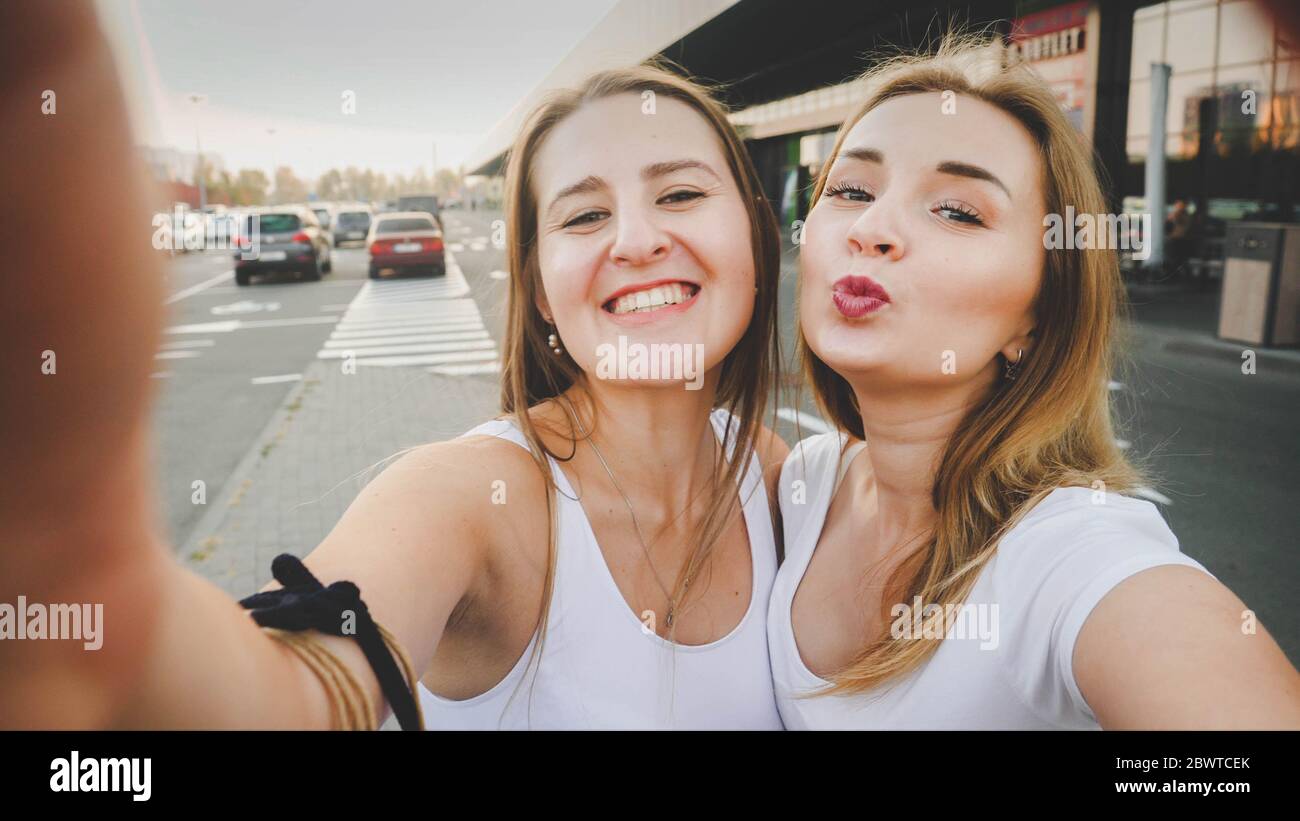 Toned selfie photo for social media of two smiling girls on car parking ...