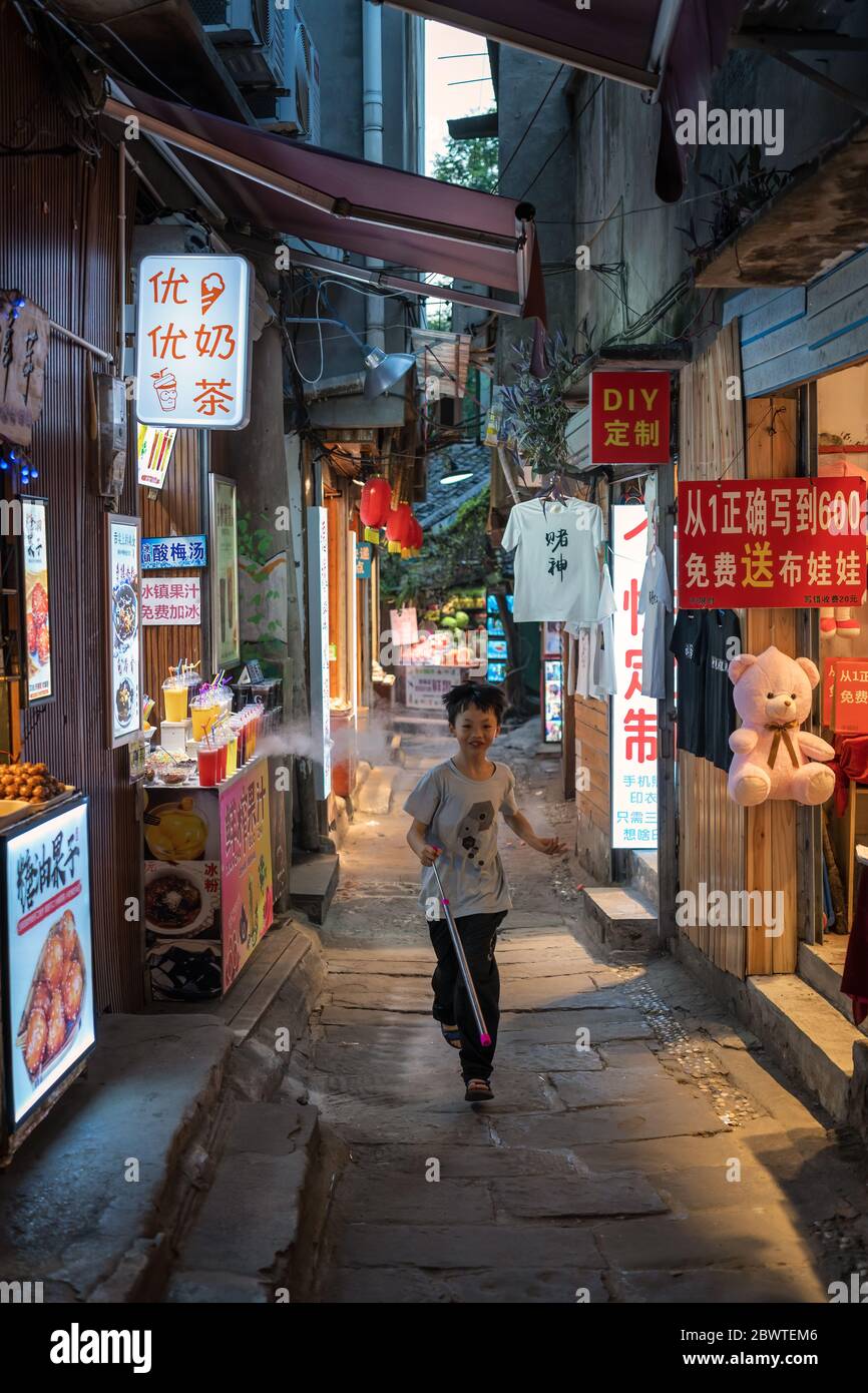 Chongqing, China -  August 2019 : Happy little boy running fast in a narrow alleway between food stalls and souvenir shops in the evening, Ci Qi Kou A Stock Photo