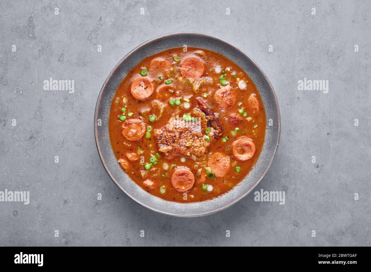 Chicken and Sausage Gumbo soup in gray bowl on concrete backdrop. Gumbo