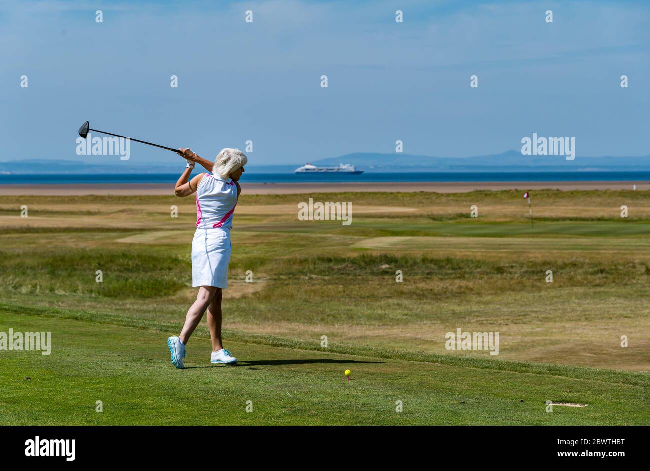 Female golfer hitting golf ball on golf course with view of Firth of Forth, East Lothian, Scotland, UK Stock Photo