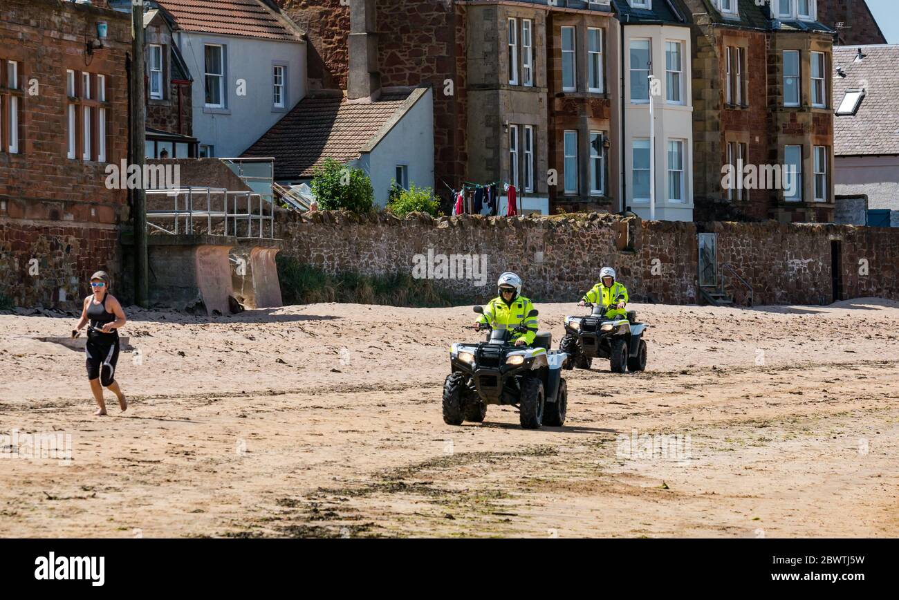 Police patrol beach on quad bikes with woman jogging, North Berwick, East Lothian, Scotland, UK Stock Photo