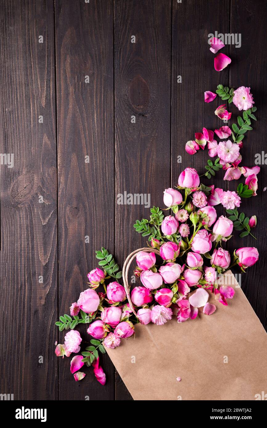 Bouquet of roses Roses in a paper bag on the wooden brown background. Top view. Copy space. Instagram style photo Stock Photo