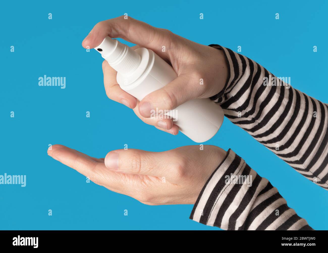 Hands using a white spray bottle, isolated against a blue background Stock Photo