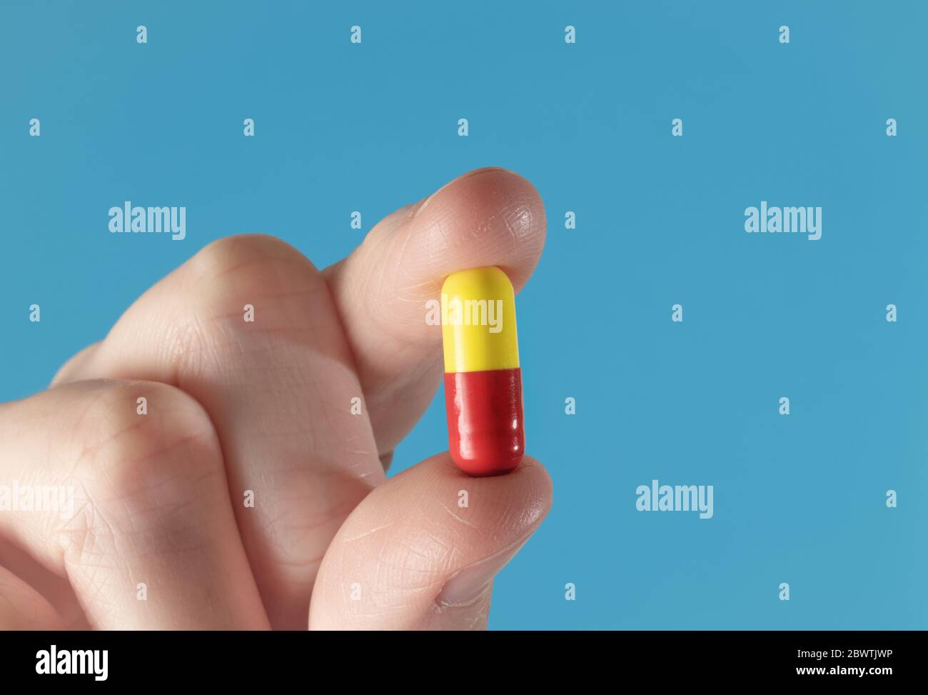 Fingers holding up a yellow and red medicine capsule. Extreme macro closeup with a blue background Stock Photo