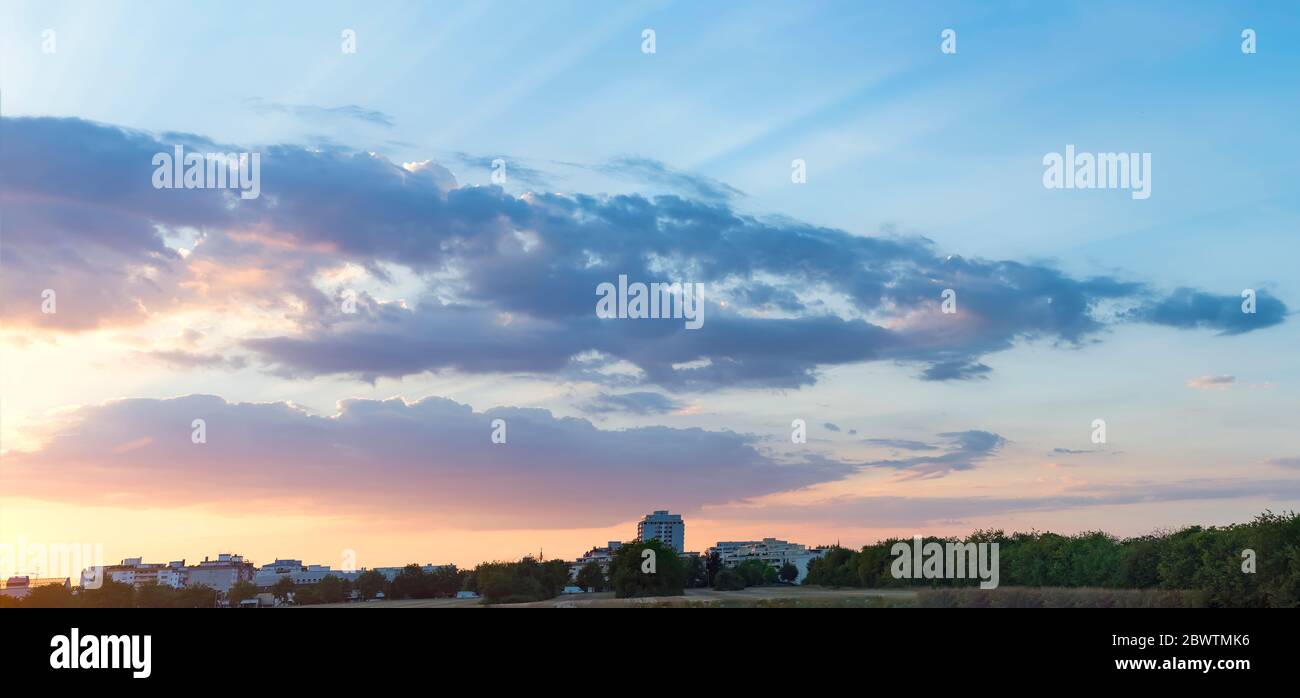 The beautiful sunset over the trees and blue sky gold sunset with natural sunlight against the backdrop of city houses and factories Stock Photo