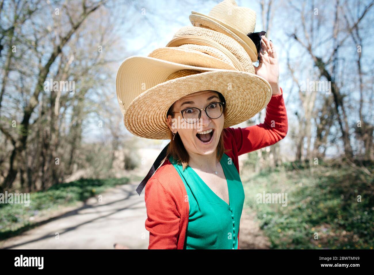 Portrait of mature woman with stack of straw hats on her head pulling funny faces Stock Photo