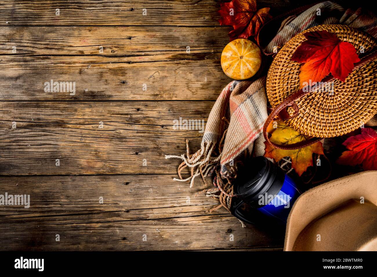 Fall cosiness rustic background. Autumn walks, garden relaxation concept. Wooden background with warm plaid, hat, wicker bag, thermos cup of tea, coff Stock Photo
