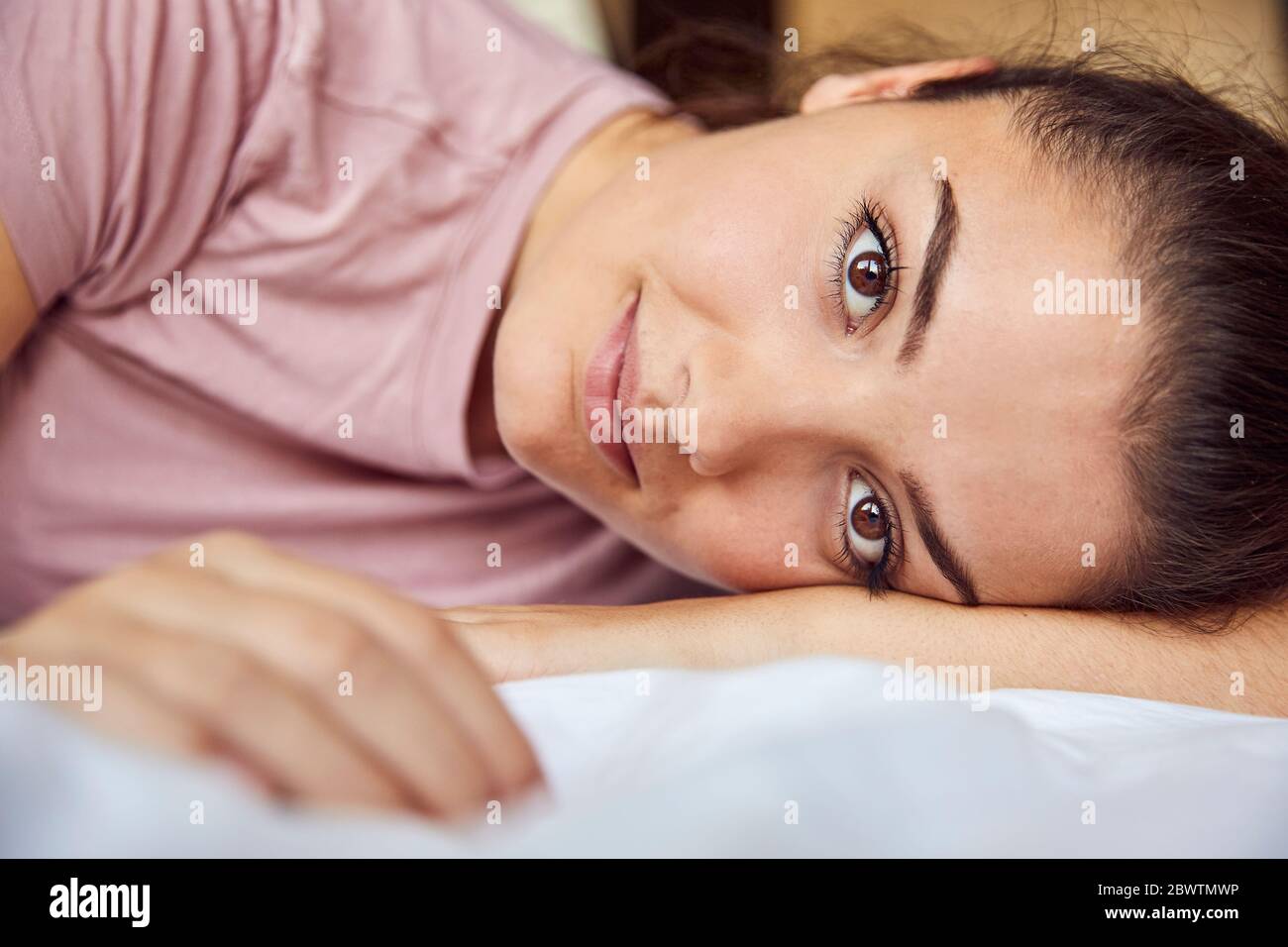 Portrait of young woman with brown eyes lying on bed Stock Photo