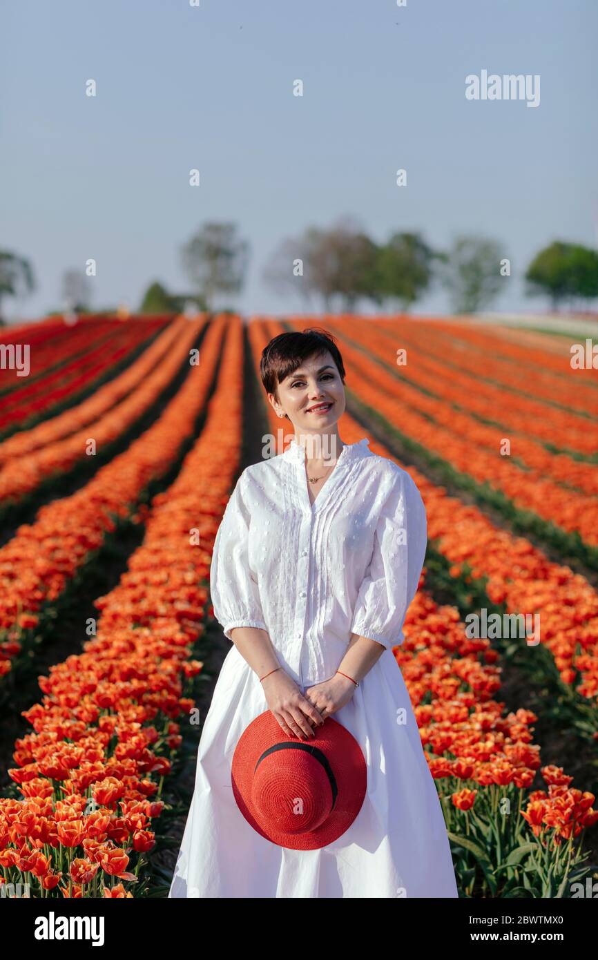 Portrait of smiling woman dressed in white standing in front of tulip field Stock Photo
