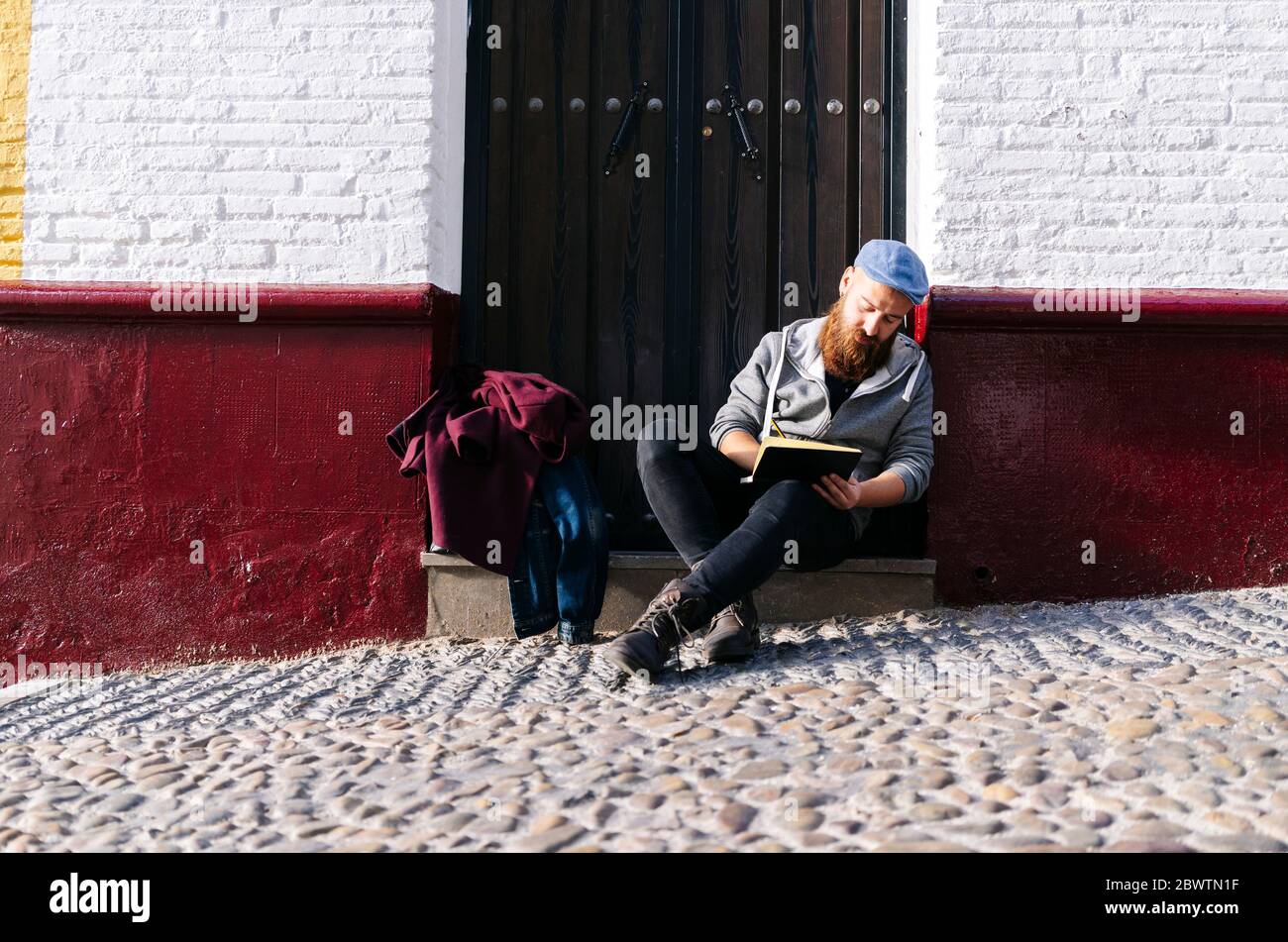 Man sitting on front stoop in the city drawing a sketch, Granada, Spain Stock Photo