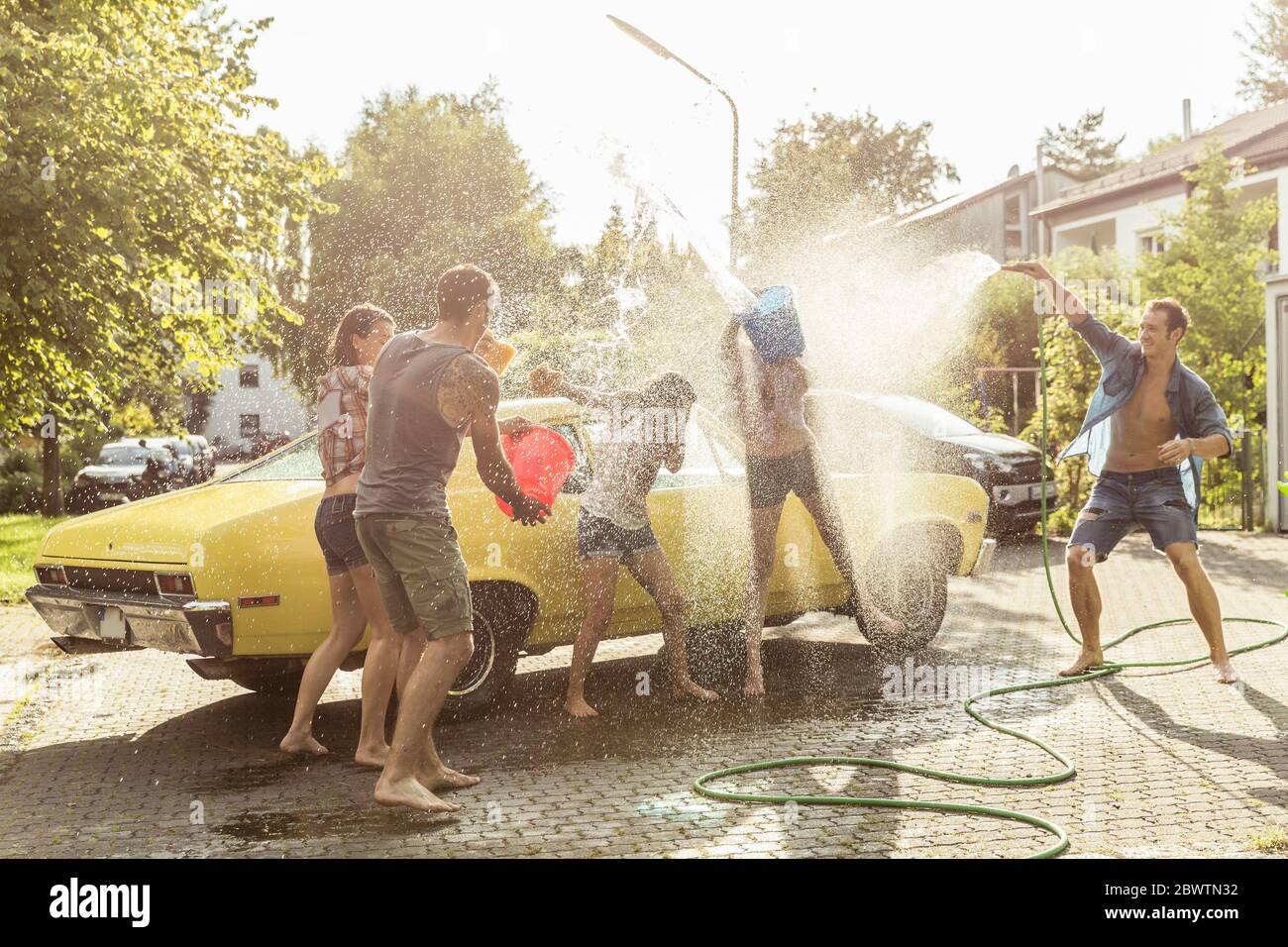 Group of friends washing yellow vintage car in summer having fun Stock Photo