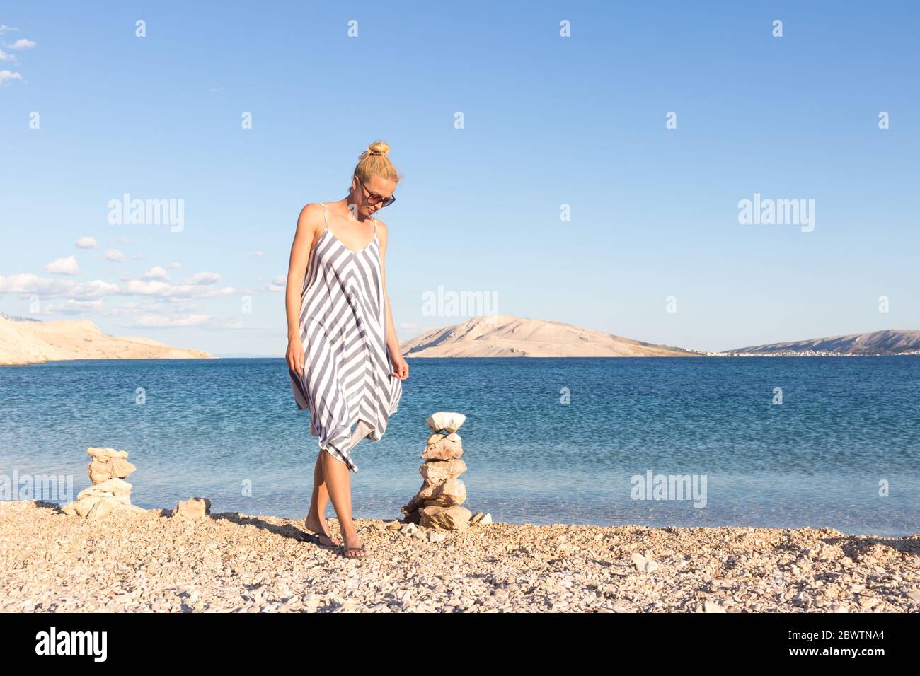 Happy carefree woman enjoying late afternoon walk on white pabbled beach on Pag island, Croatia Stock Photo