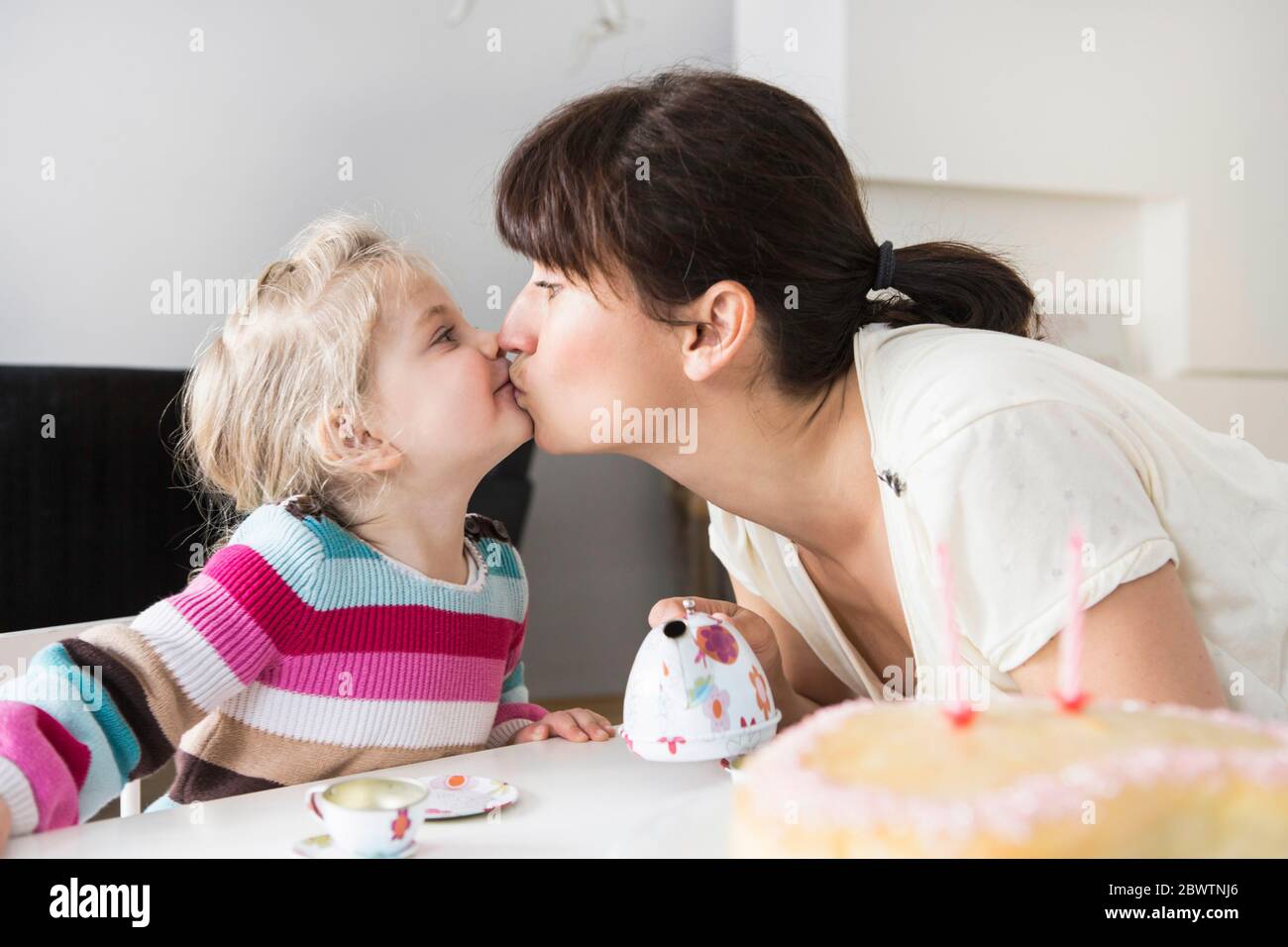Mother and daughter playing with doll's china set, kissing each other Stock Photo