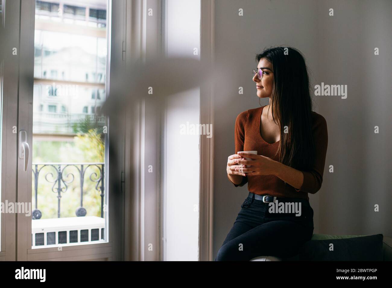 Thoughtful looking through window while enjoying coffee at office during break Stock Photo