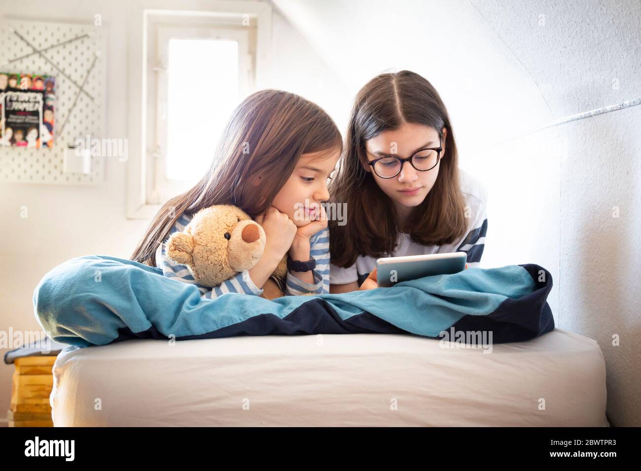 Sisters using tablet lying on bed Stock Photo