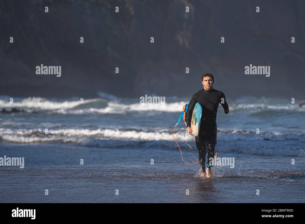 Handicapped surfer with surfboard running at beach Stock Photo