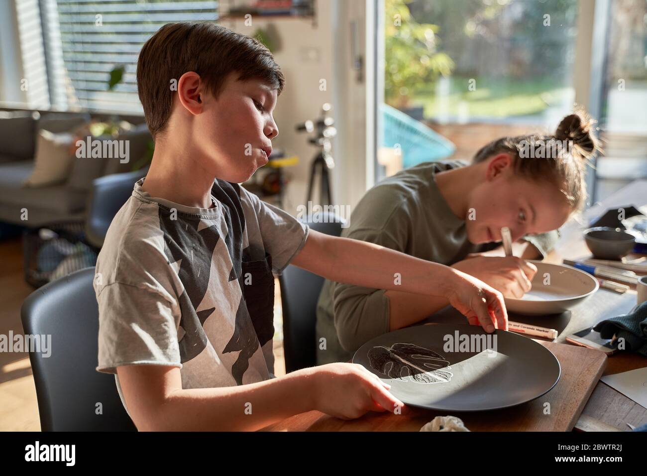 Brother and sister at home painting crockery with porcelain paint Stock