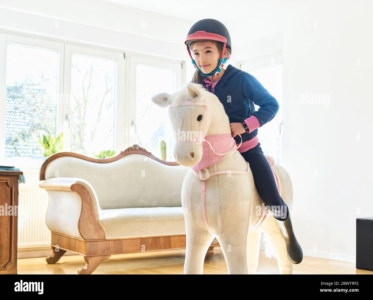 Girl riding on play horse at home Stock Photo