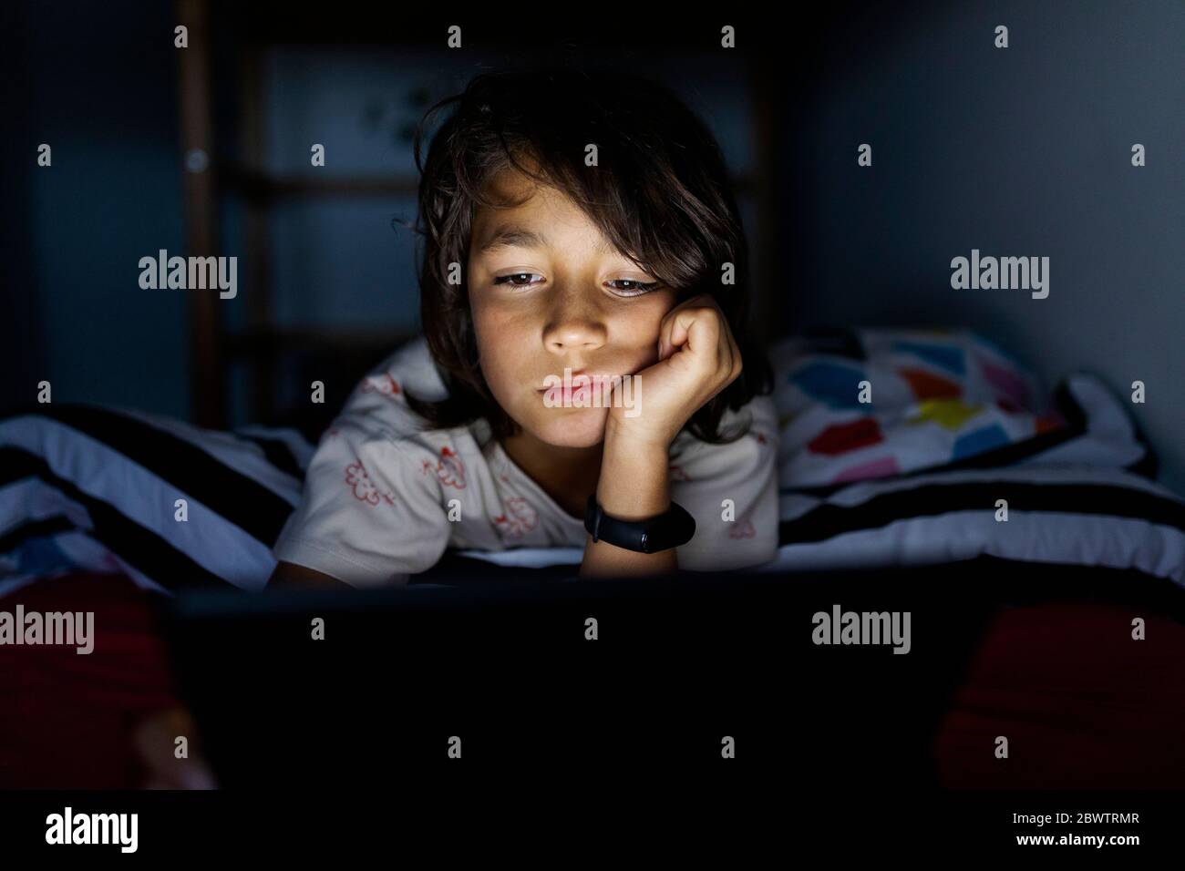 Portrait of bored boy lying on bed at home using digital tablet Stock ...