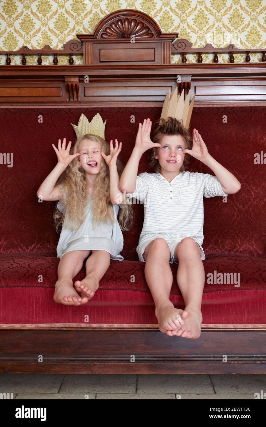 Boy and girl sitting on a couch wearing cardboard crowns messing about Stock Photo