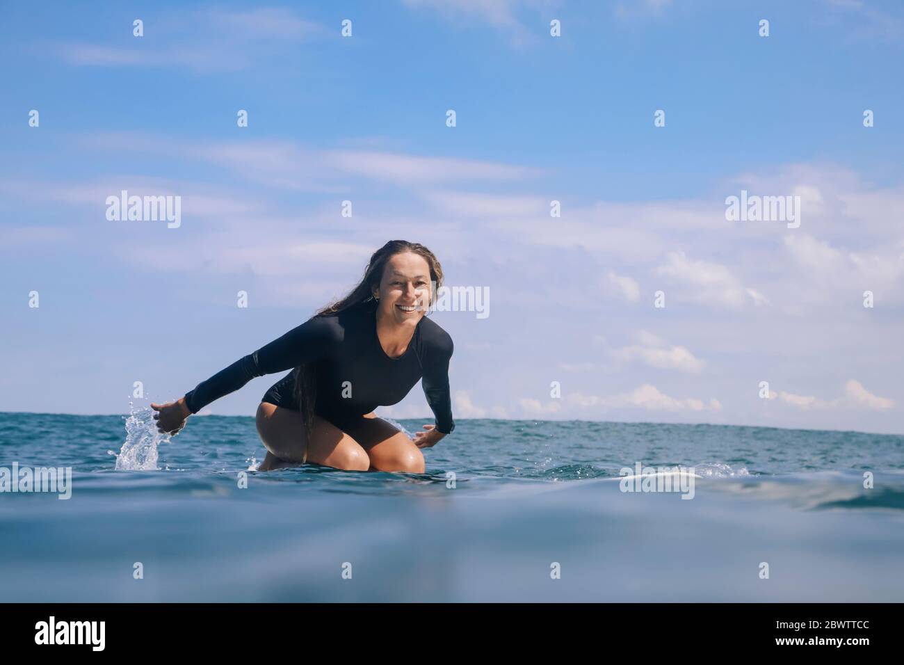 Portrait of a happy woman kneeling on surfboard in the sea, Bali, Indonesia Stock Photo