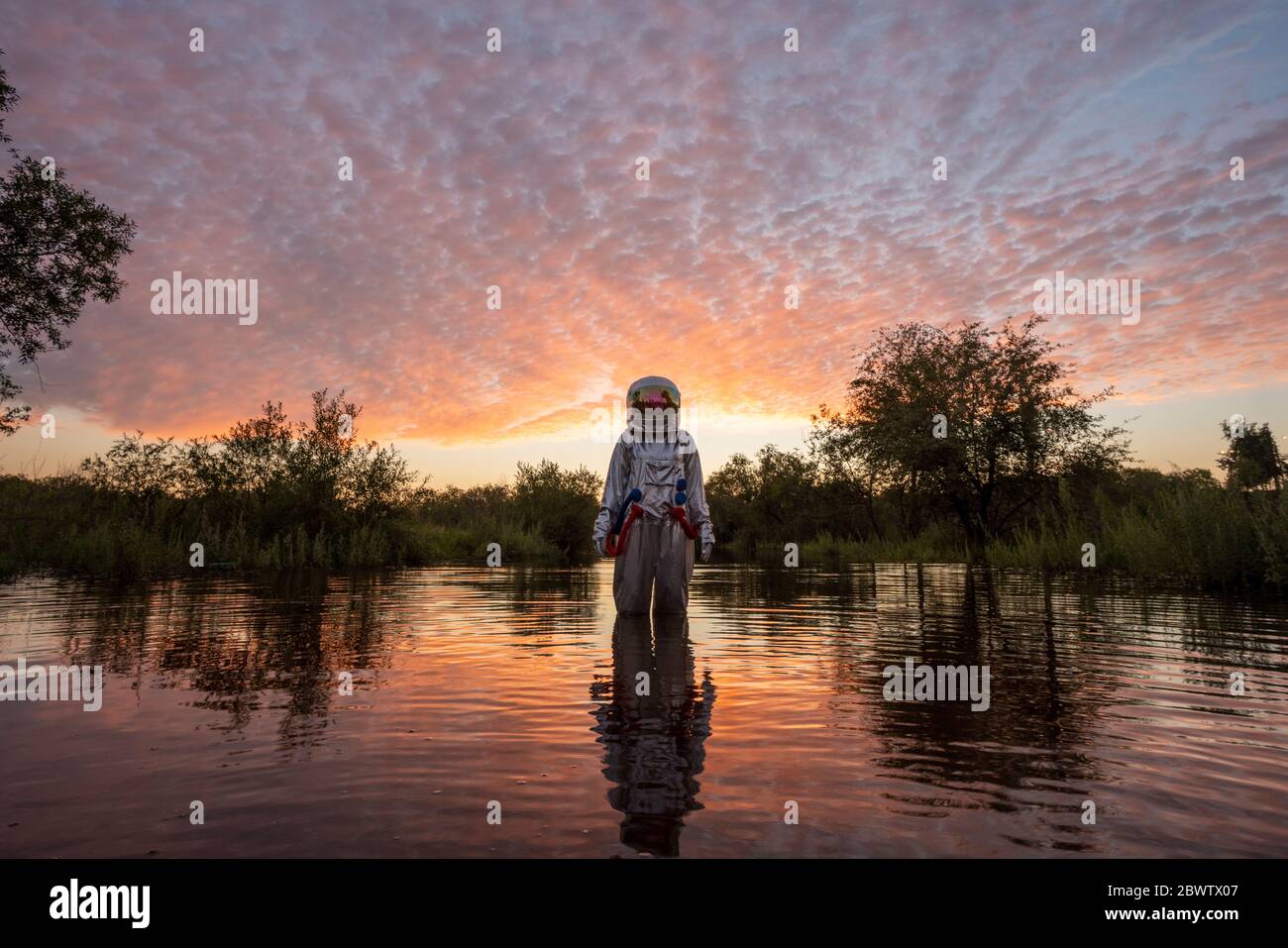 Spacewoman standing in water at sunset Stock Photo