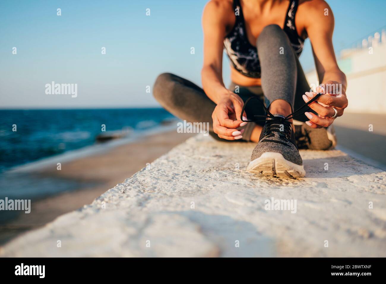 Low section of young woman tying shoelace on promenade Stock Photo