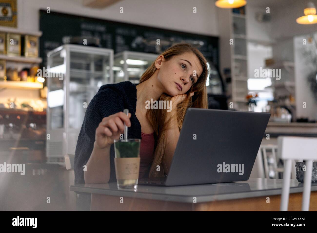 Daydreaming young woman with laptop in a cafe Stock Photo