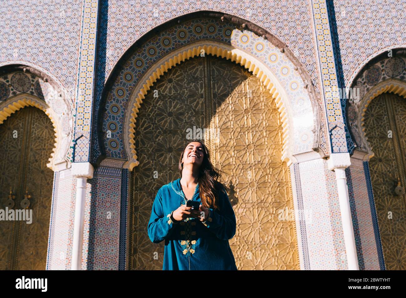 Young woman standing in front of traditional architure wearing Moroccan robe, Morocco Stock Photo