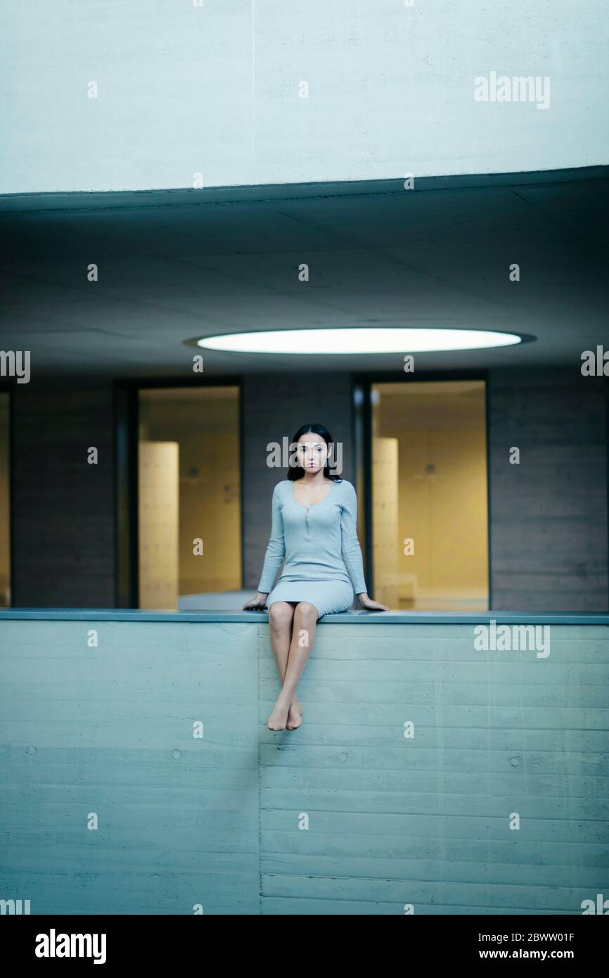 Thoughtful woman sitting on concrete wall Stock Photo - Alamy