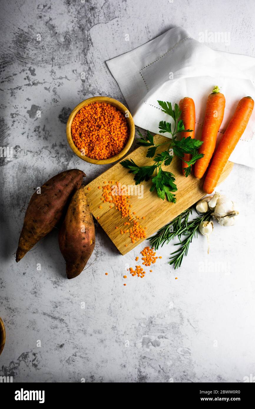 Studio shot of cutting board, bowl of red lentils, sweet potatoes, carrots, rosemary, parsley and garlic Stock Photo