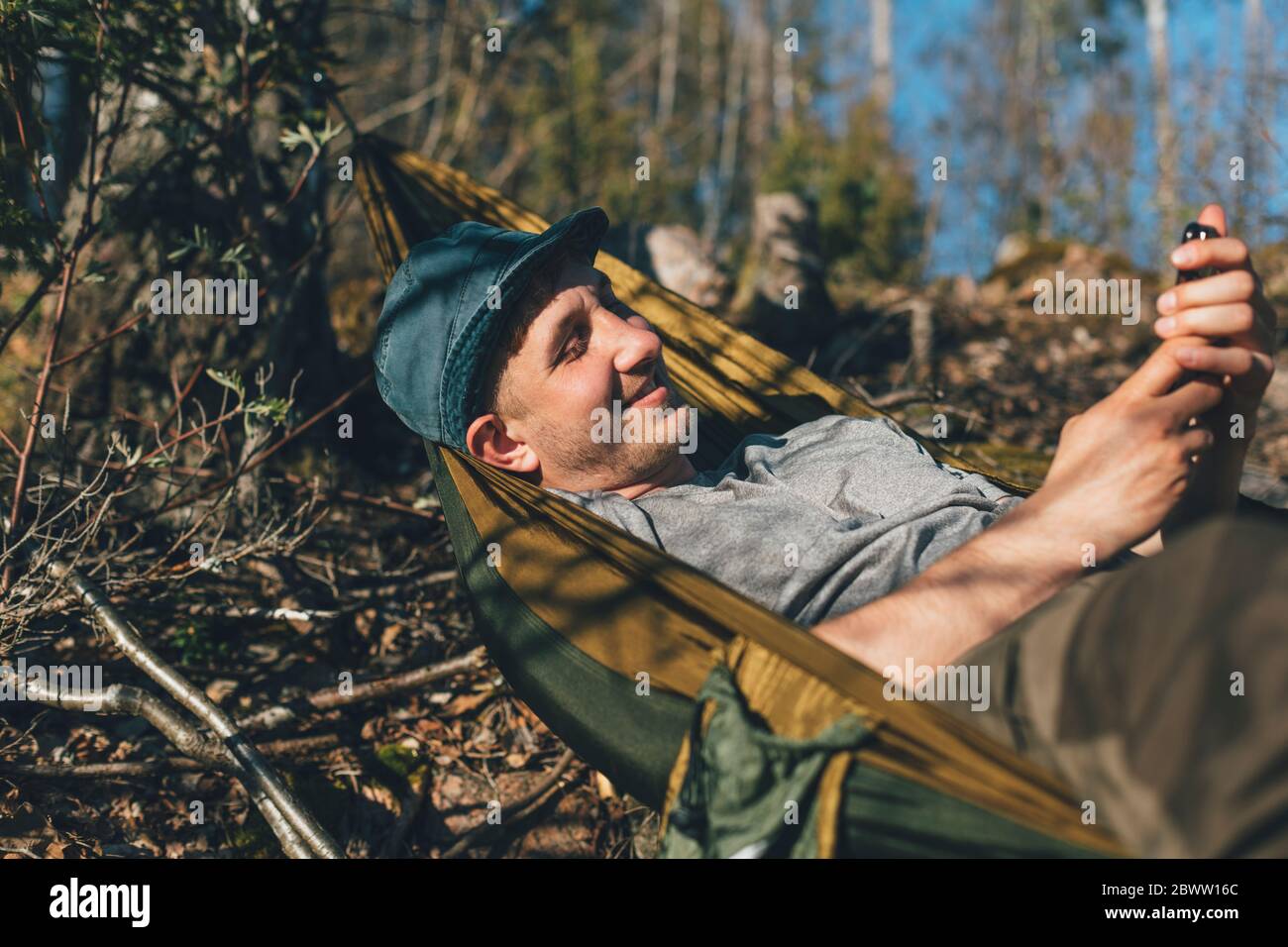 Young man relaxing in hammock, using smartphone Stock Photo