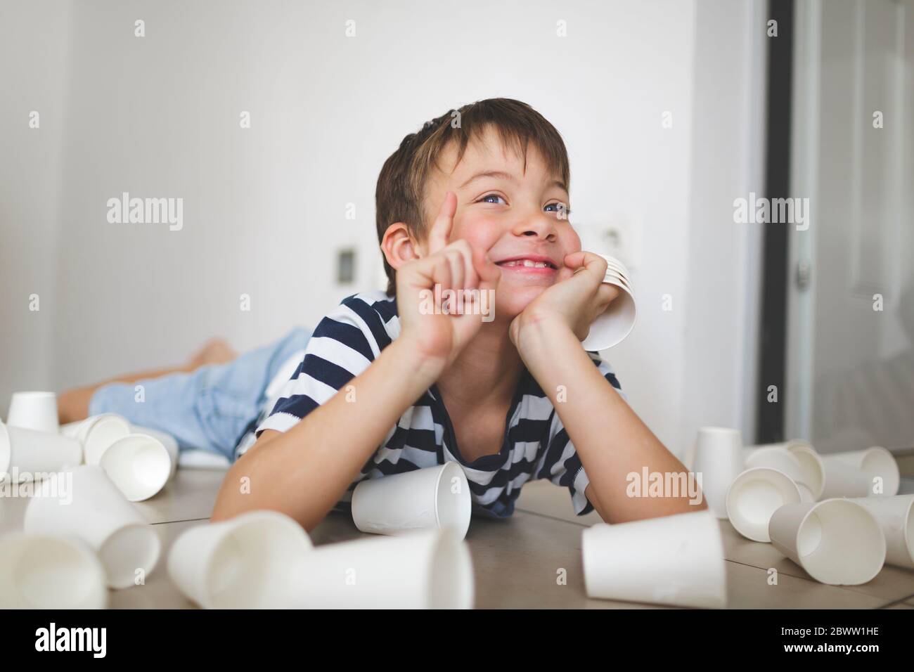 Portrait of smiling little boy lying on the floor between white paper ...