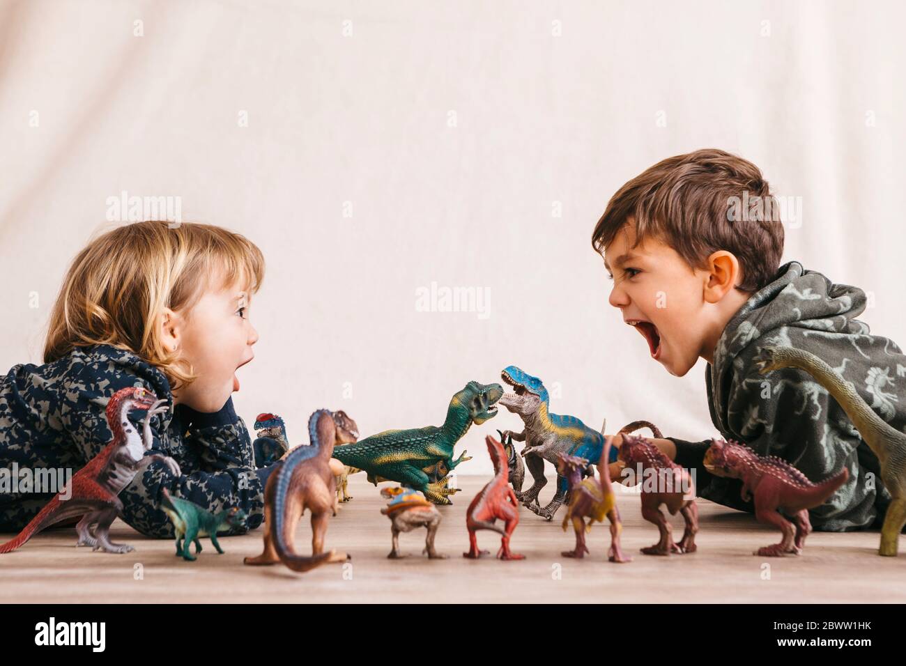 Brother and his little sister playing with toy dinosaurs Stock Photo