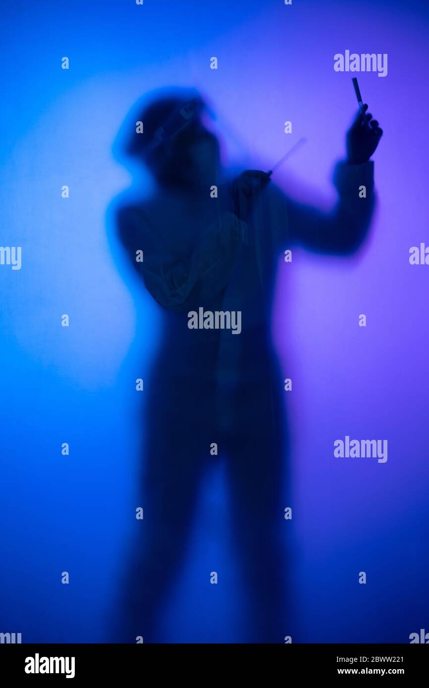 Woman in protective wear behind translucent glasspane holding specimen Stock Photo
