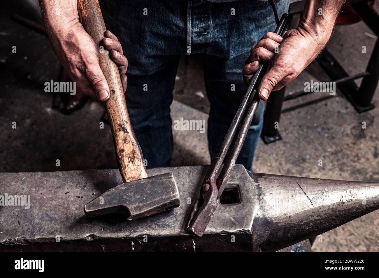 Knife maker holding pliers and hammer on anvil Stock Photo