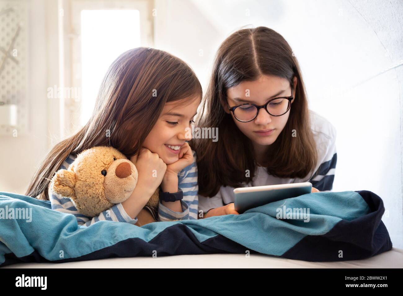 Sisters using tablet lying on bed Stock Photo