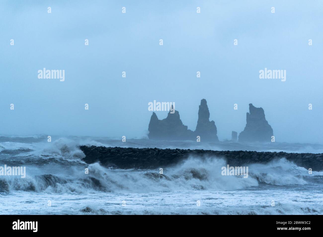 Iceland, Hofn, Sea waves splashing against coastal stone wall with stack rocks in background Stock Photo