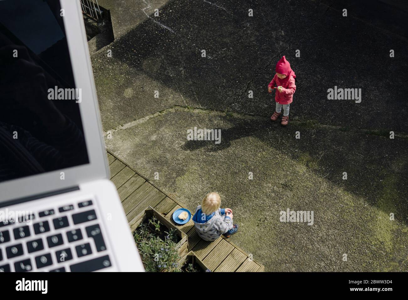 Siblings playing together on courtyard wit laptop in foreground Stock Photo