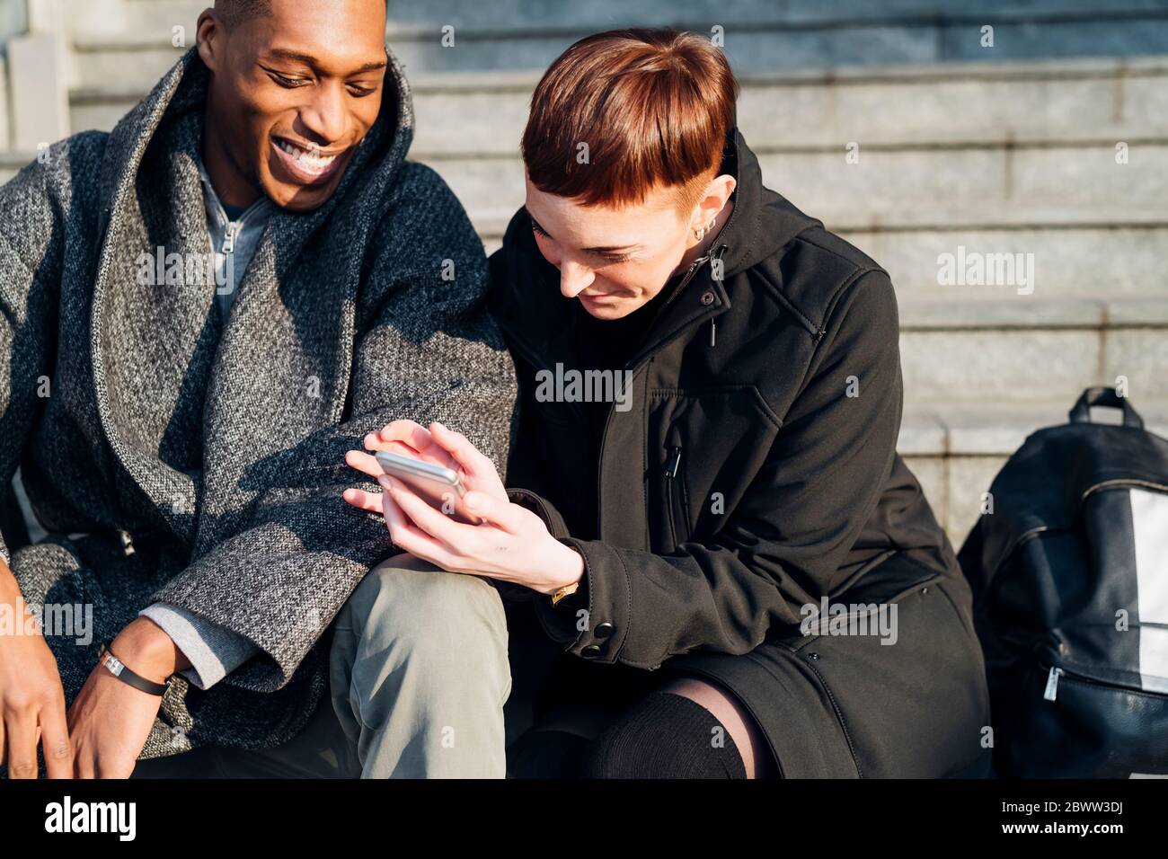 Happy young couple in the city sitting on stairs using cell phone Stock Photo