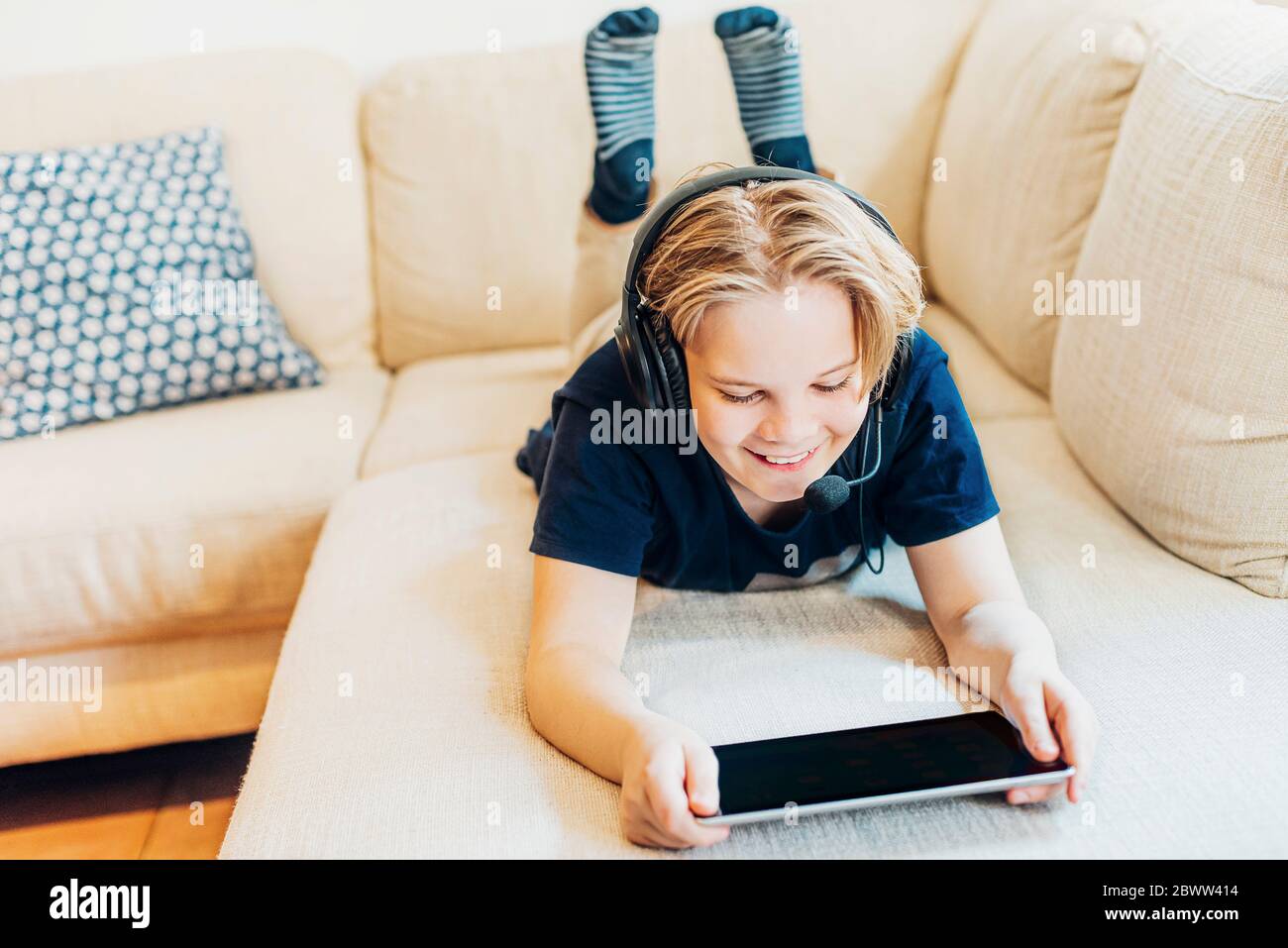 Boy lying on couch at home with headset and tablet Stock Photo - Alamy